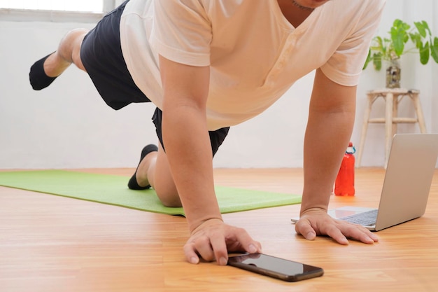 Hombre con tableta haciendo ejercicio de tablón en casa