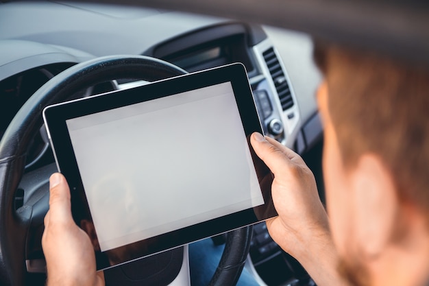 Un hombre con una tableta en la mano al volante del coche.