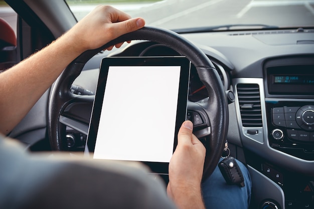 Un hombre con una tableta en la mano al volante del coche.