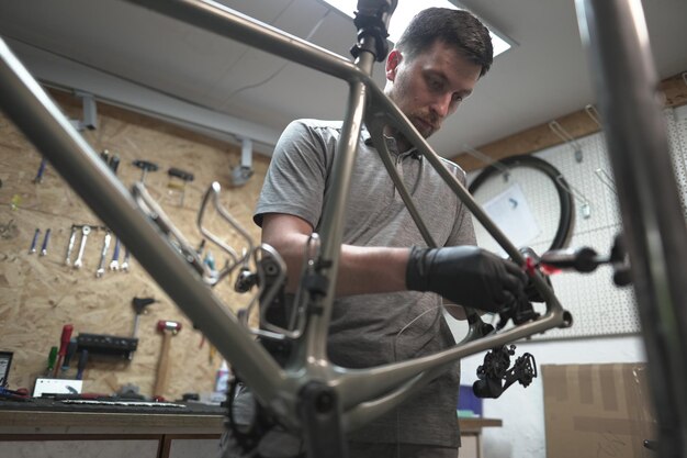 Foto un hombre está en un taller centrándose en un marco de bicicleta cerca están los neumáticos de automóviles piezas de bicicleta y