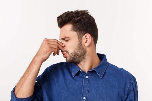 Hombre tapándose la nariz contra un mal olor aislado sobre gris