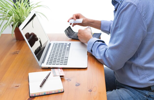 Hombre con tarjeta de crédito frente a la computadora.