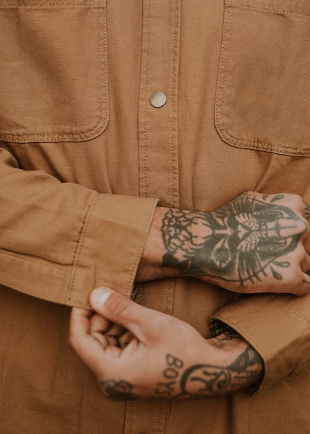 Hombre tatuado abotonarse la camisa marrón closeup
