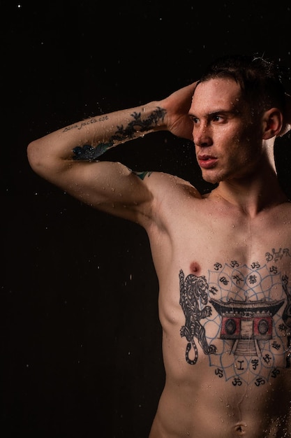 Hombre tatuado saludable sexy con gotas de agua en su cuerpo Retrato de estudio masculino de moda de torso desnudo