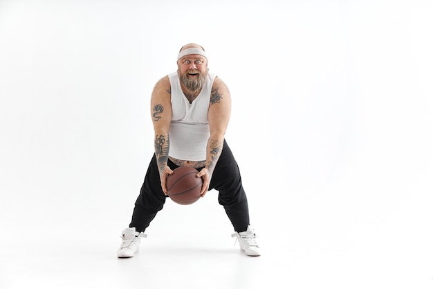 Hombre tatuado con sobrepeso barbudo con pelota de baloncesto en fondo blanco.
