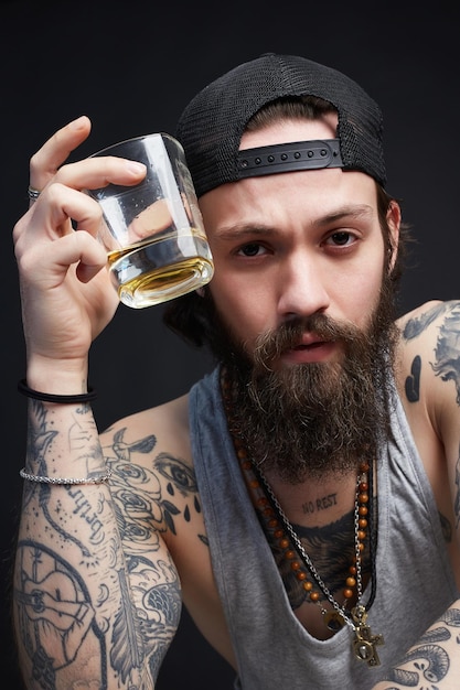 Hombre tatuado con sombrero bebiendo un whisky