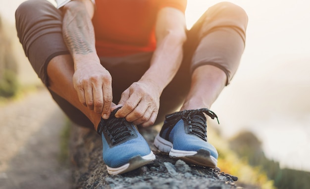 El hombre del tatuaje en forma ata sus zapatos deportivos al aire libre durante la sesión de jogging