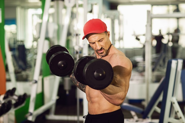 Un hombre con un tatuaje en un gimnasio. Ejecute ejercicio con pesas en un gimnasio colorido