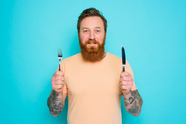 Hombre con tatuajes está listo para comer con cubiertos en mano