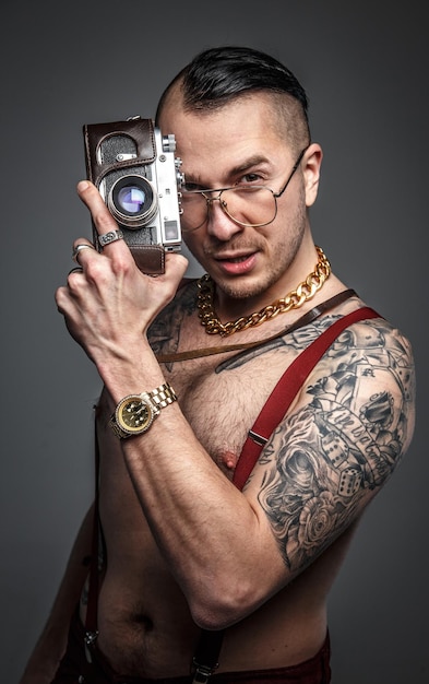 Hombre con tatuajes en su cuerpo con cámara de fotos. Aislado en gris.