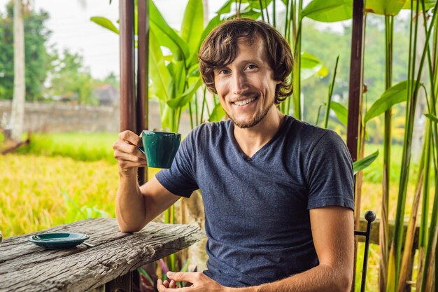 Hombre con una taza de café en la terraza del café cerca de las terrazas de arroz en Bali, Indonesia.