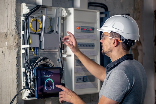 Foto el hombre, un técnico eléctrico que trabaja en un cuadro de distribución con fusibles, usa una tableta