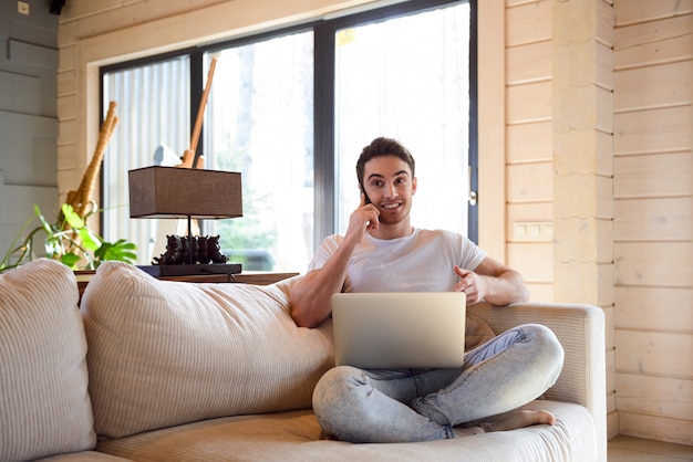 Hombre con teléfono y computadora portátil en casa