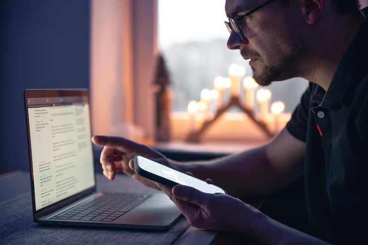 Foto un hombre con un teléfono inteligente se sienta frente a una computadora portátil a altas horas de la noche