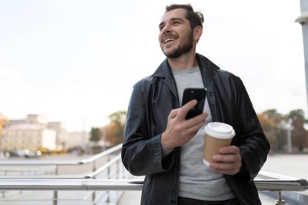 Un hombre con un teléfono móvil en la ciudad tomando café.