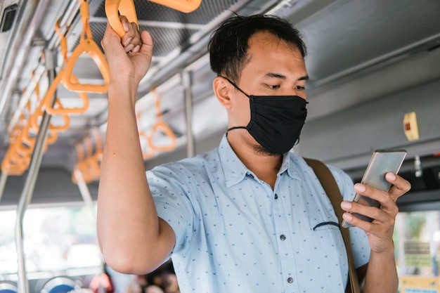Hombre con teléfono móvil mientras está de pie en el transporte público use máscara