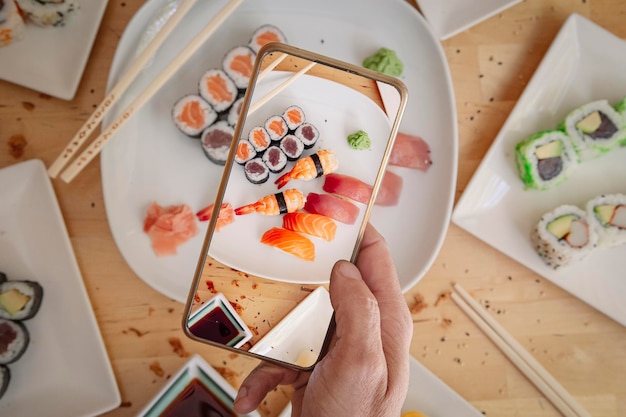 Hombre con teléfono móvil tomando fotos de delicioso sushi en la vista superior de la mesa