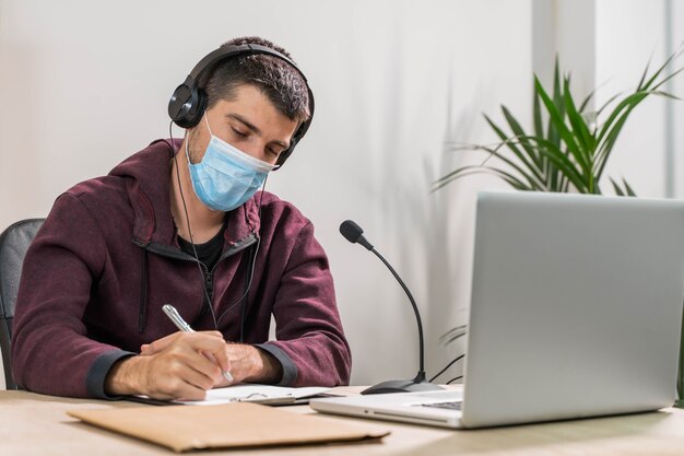 Hombre de telemarketer o podcast que trabaja con un portátil y hablando por un auricular con mascarilla en la oficina