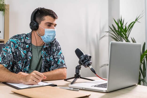 Foto hombre de telemarketer o podcast que trabaja con un portátil y hablando por un auricular con mascarilla en la oficina