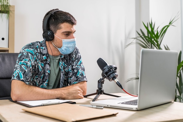 Hombre de telemarketer o podcast que trabaja con un portátil y hablando por un auricular con mascarilla en la oficina