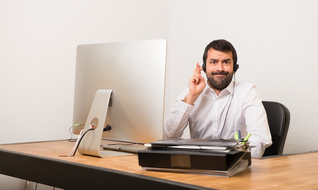 Hombre de telemarketer en una oficina con los dedos cruzando y deseando lo mejor.