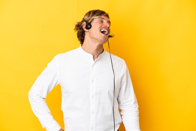 Hombre de telemarketer que trabaja con un auricular aislado sobre fondo amarillo riendo