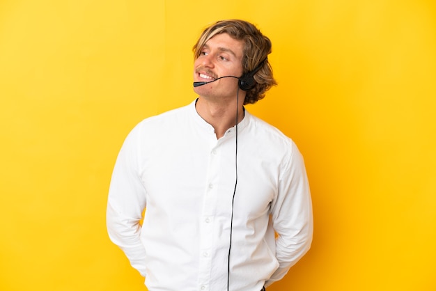 Hombre de telemercadeo que trabaja con un auricular aislado en la pared amarilla mirando hacia el lado y sonriendo