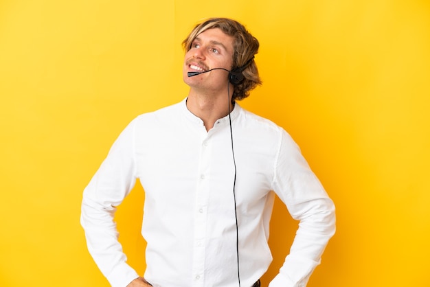 Hombre de telemercadeo que trabaja con un auricular aislado en la pared amarilla pensando en una idea mientras mira hacia arriba