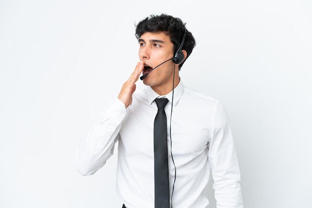 Hombre de telemercadeo que trabaja con un auricular aislado sobre fondo blanco bostezando y cubriendo la boca abierta con la mano