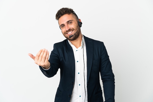 Hombre de telemercadeo que trabaja con un auricular aislado sobre fondo blanco que invita a venir con la mano. Feliz de que hayas venido