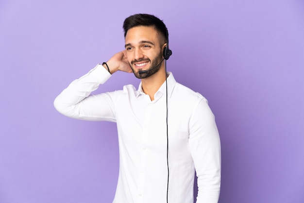 Hombre de telemercadeo que trabaja con un auricular aislado sobre fondo púrpura que tiene dudas