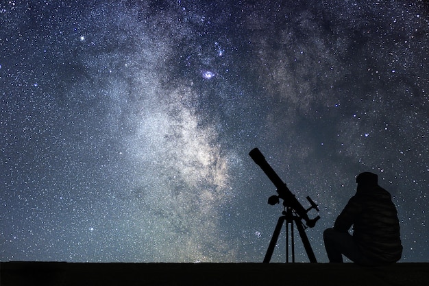 Hombre con telescopio de astronomía mirando las estrellas. Telescopio de hombre y cielo estrellado. Cielo nocturno. Via Láctea.