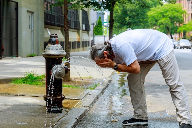 El hombre durante una temperatura de calor fuerte se refresca con agua de hidrante de fuego