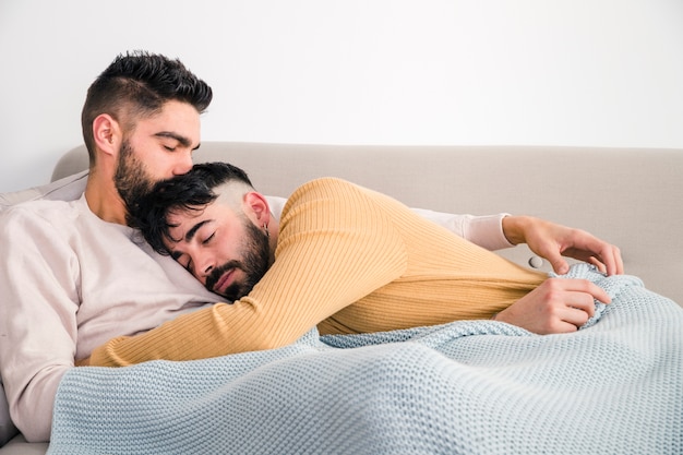 Hombre tendido en el pecho de su novio sobre el sofá contra la pared blanca