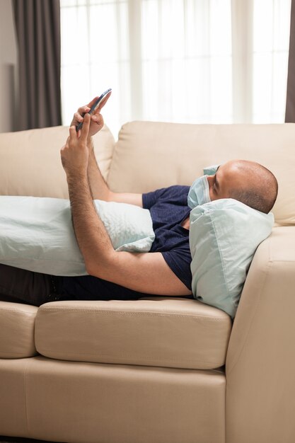 Hombre tendido en el sofá con su teléfono inteligente durante la pandemia mundial.