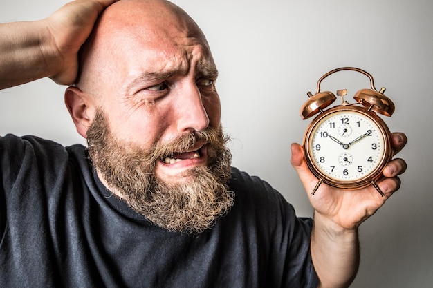 Hombre tenso mirando el despertador contra un fondo gris