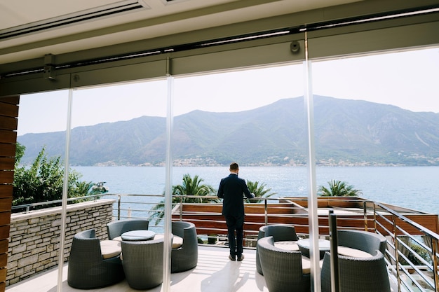 El hombre se para en la terraza de un hotel de lujo y mira a la vista posterior del mar