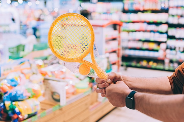 Un hombre en una tienda selecciona un juego de tenis para niños y sostiene una raqueta de tenis en sus manos.