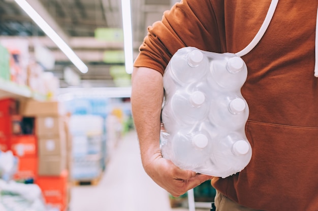 Un hombre en una tienda sostiene un paquete de agua embotellada limpia y transparente.