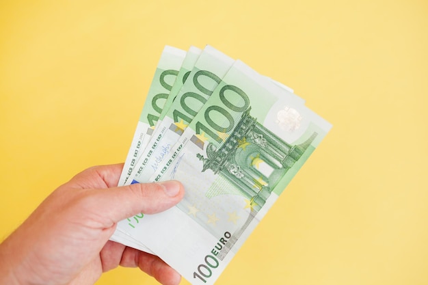 Un hombre tiene billetes de 100 euros en la mano con un fondo amarillo. efectivo papel moneda, pago