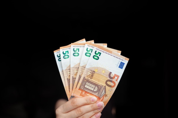Un hombre tiene billetes de 100 euros en la mano sobre un fondo oscuro