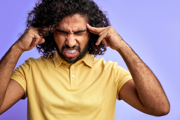 El hombre tiene dolor de cabeza aislado, sostenga la cabeza con la mano, dolor en la sien, párese con los ojos cerrados aislado sobre el espacio púrpura