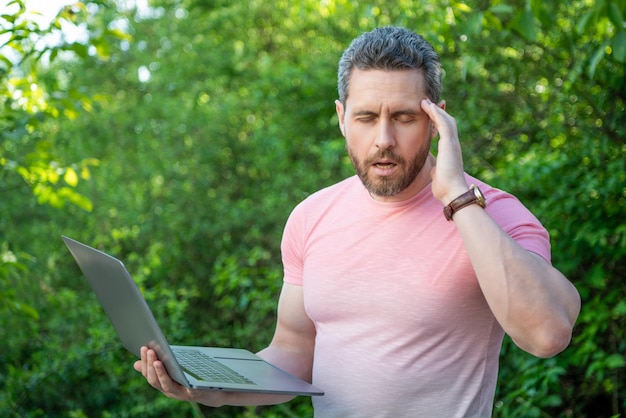 El hombre tiene dolor de cabeza después de hacer negocios en línea al aire libre el hombre tiene negocios en línea en la computadora portátil