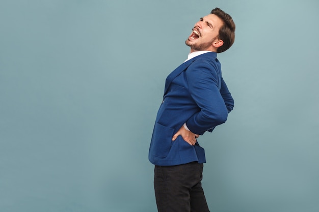 El hombre tiene dolor de espalda. Piedras u órganos renales. Retrato de hombre de negocios guapo con barba en traje azul y camisa blanca. Tiro de estudio interior, aislado sobre fondo azul claro