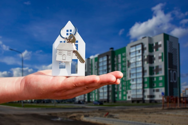 El hombre tiene las llaves de la casa en sus manos con el telón de fondo de un edificio de varios pisos. Concepto de compra y alquiler de apartamentos.