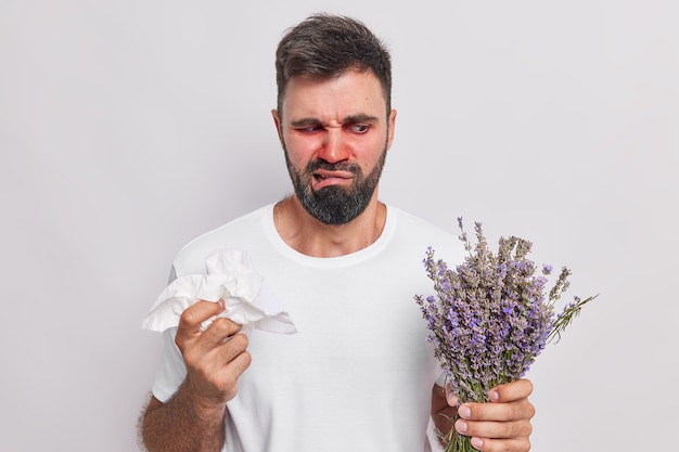 El hombre tiene una reacción alérgica a la lavanda tiene un pañuelo para limpiarse la nariz tiene los ojos rojos y lleva una camiseta casual aislado en blanco