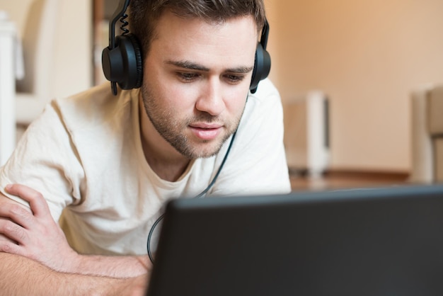 Hombre tirado en el suelo usando auriculares en la computadora portátil