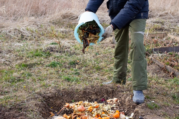 El hombre tirando las sobras de frutas y verduras para el compostaje al aire libre en el jardín