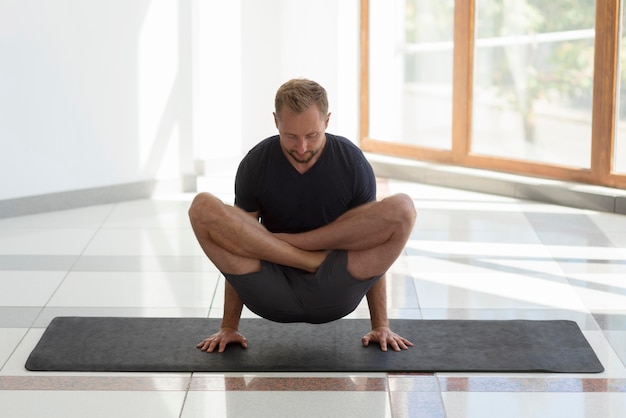 Hombre de tiro completo practicando yoga en interiores