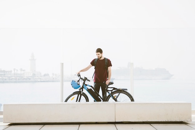 Foto hombre de tiro largo de pie junto a la bicicleta eléctrica